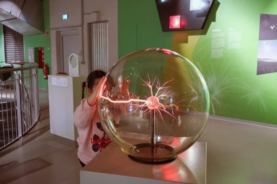 Anak menyentuh bola plasma di pameran sains